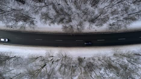 Birdseye-Aerial-View-of-Cars-on-Wet-Road-and-Snowy-Countryside-Landscape