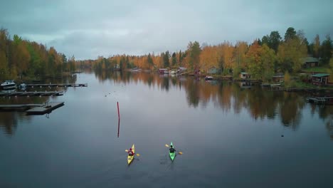 Tourists-enjoying-scenic-fall-colors-lining-calm-river-on-kayaking-tour,-Finland