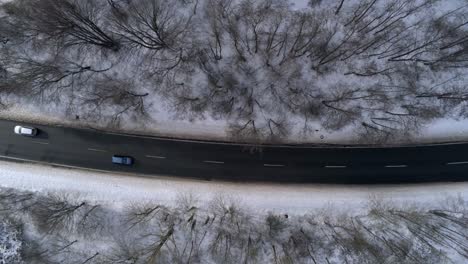 Top-down-zoom-in-drone-view,-cars-on-barren-snowy-winter-forest-road