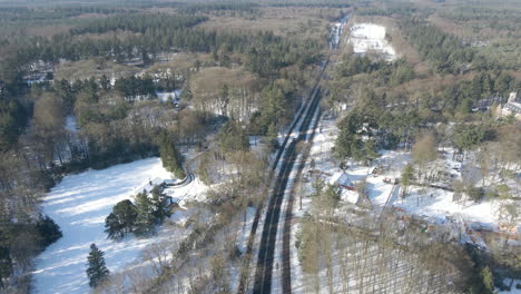 High-aerial-of-truck-driving-over-empty-road-surrounded-by-forest-in-winter