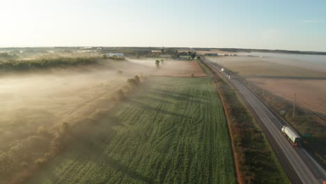 Morning-mist-and-low-fog-blanket-farm-fields-and-rural-highway-with-light-traffic