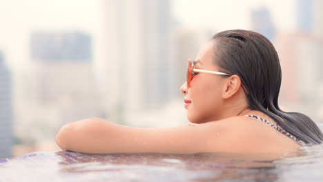 Close-Up-of-Young-Asian-Woman-on-Rooftop-Infinity-Pool-With-Amazing-View-of-City-in-Background,-Full-Frame
