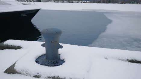 Mooring-Bollard-On-Snowy-Quay-With-Ice-On-Water-In-Bakcground-At-Wintertime