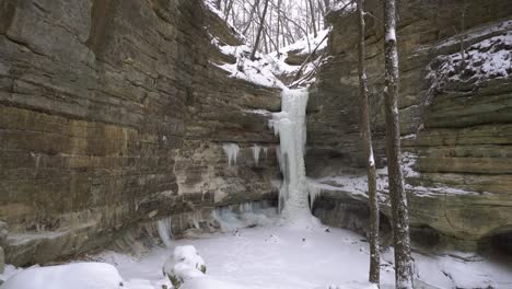 Natural-cliff-and-frozen-waterfall-during-light-snowfall,-winter-season