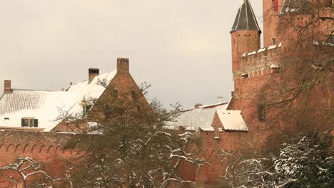 Pan-showing-the-remains-of-the-medieval-city-wall-revealing-the-Drogenapstoren-rising-above-winter-barren-trees-part-of-the-cityscape-of-Hanseatic-city-Zutphen,-The-Netherlands,-covered-in-snow