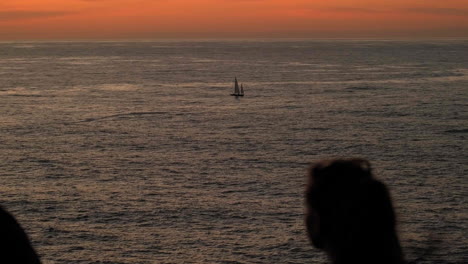 Silhouette-Von-Menschen,-Die-Den-Sonnenuntergang-Und-Den-Ruhigen-Ozean-Mit-Einem-Einsamen-Segelboot-Genießen