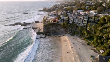 Beautiful-sandy-beach-with-waves-of-pacific-ocean-reaching-shore-and-luxury-buildings-on-top-of-cliff
