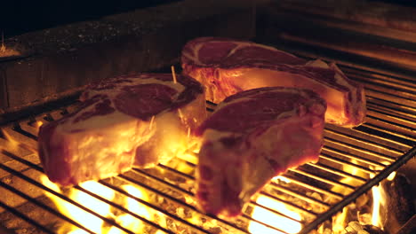 Three-thick-steaks-grilling-on-rack-over-open-flames-from-wood-fire