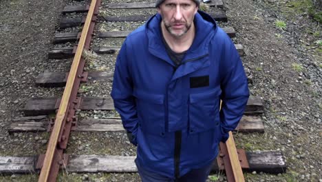 Male-walking-on-train-tracks-alone,-serious-look,-aerial-tracking-view