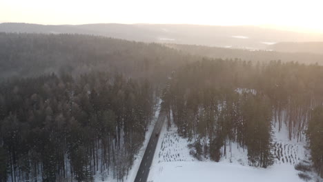 Aerial-Shot-Of-Car-Driving-Through-Snow-Covered-Forest-At-Sunset,-Beautiful-Winter-Scene