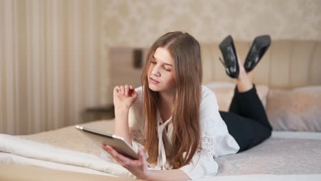 Young-beautiful-woman-in-business-style-lying-in-bed-flipping-through-a-tablet