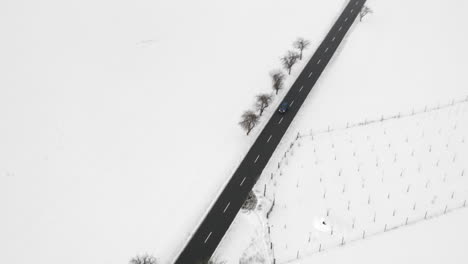 Aerial-Shot-Of-A-Car-Driving-On-A-Rural-Road,-Winter-Snow-Covered-Landscape