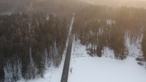 Aerial-Shot-Of-Road-In-Beautiful-Mountain-Forest,-Snow-Covered-During-Winter-At-Sunrise