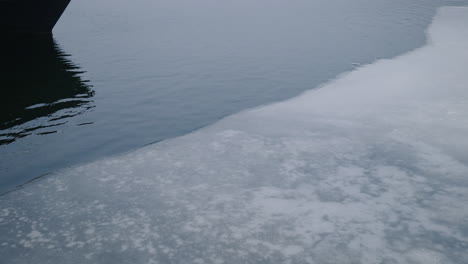 Frozen-Lake-With-Reflection-Of-Boat's-Bottom-Edge-Near-Shoreline-During-Winter