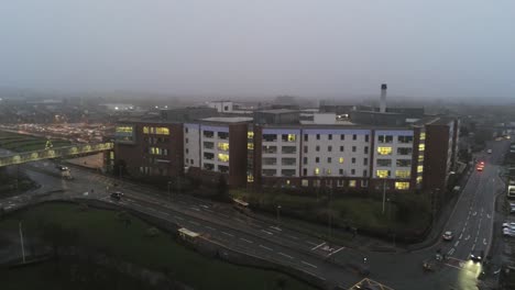 Aerial-view-British-NHS-hospital-on-misty-wet-damp-morning-rising-tilt-down-shot