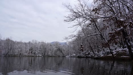Beautiful-lake-with-calm-cold-water-reflecting-forest-trees-covered-in-white-snow