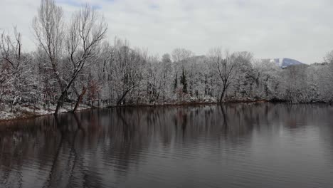 Paradise-winter-landscape-with-calm-lake-surrounded-by-park-trees-covered-in-snow