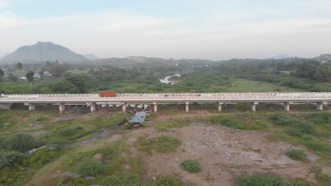 Aerial-view-over-a-green-vast-field-in-India,-flying-above-overlooking-a-road-bridge-with-cars-driving-on-it,-wide-shot,-transportation-concept