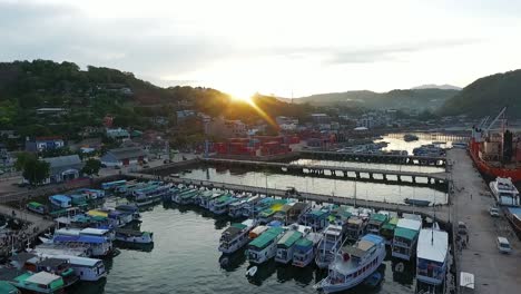 Aerial-view-overlooking-boats,-at-the-Labuan-Bajo-fishing-town,-sunset,-in-Flores,-Indonesia---pan,-drone-shot