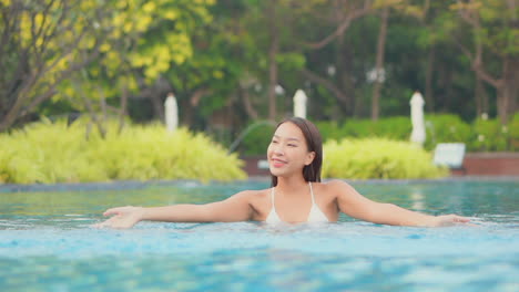 Smiling-Asian-girl-in-pool-plays-with-water