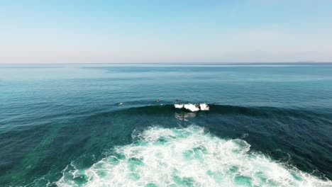 Aerial-drone-view-following-surfers,-catching-a-wave,-in-clear-waters-of-Indonesia