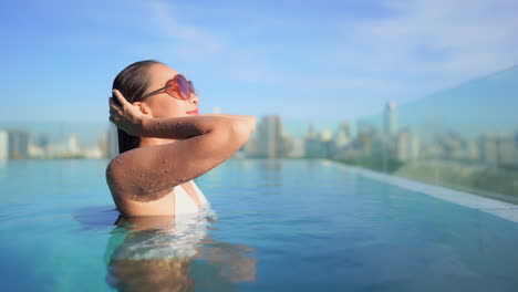 A-beautiful-young-woman-fresh-from-a-swim-in-a-rooftop-resort-infinity-edge-pool-looks-out-over-the-city-skyline