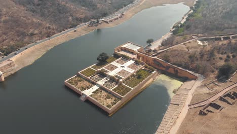 Kesar-Kyari-Bagh-garden-on-Maota-Lake,-right-before-Amber-Fort,-in-Jaipur,-Rajasthan,-India---Aerial-Wide-Orbit-shot