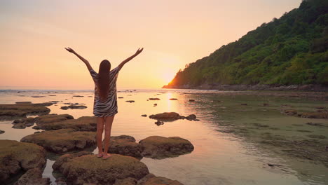 Lonely-woman-enjoying-in-sunset-sunlight-on-exotic-tropical-beach,-raising-hands-in-the-air,-static-slow-motion