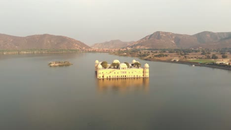 Serene-Jal-Mahal-Tendido-En-Medio-Del-Lago-Man-Sagar-En-Jaipur,-Rajasthan,-India---Toma-Panorámica-Aérea-De-órbita-Amplia