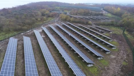 Solar-panel-array-rows-aerial-view-misty-autumn-woodland-countryside-fly-over