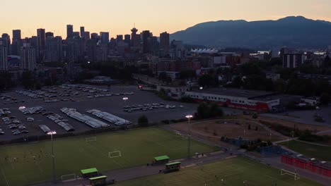 Sunset-Drone-Aerial-shot-with-football-ground-and-sun-setting-behind-cityscape-North-Vancouver-British-Columbia,-Canada