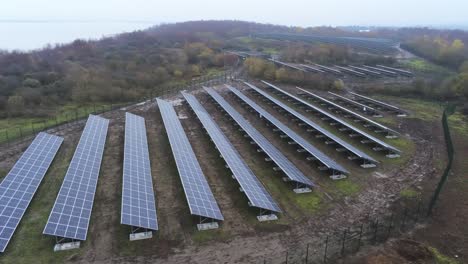 Solar-panel-array-rows-aerial-view-misty-autumn-woodland-countryside-slow-left-dolly-back