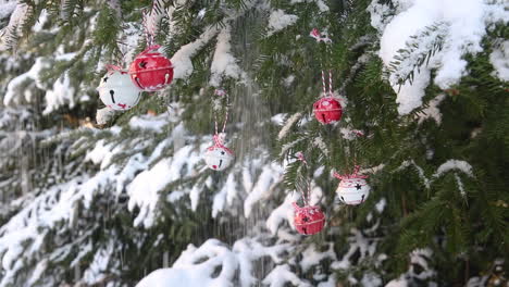 Snowfall-from-spruce-branches,-bell-baubles-decoration,-outdoor-Christmas-tree