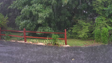 Ein-Starker-Regen,-Der-Während-Eines-Gewitters-Mit-Einem-Verschütteten-Schienenzaun-Im-Hintergrund-Auf-Die-Auffahrt-Draußen-Fällt