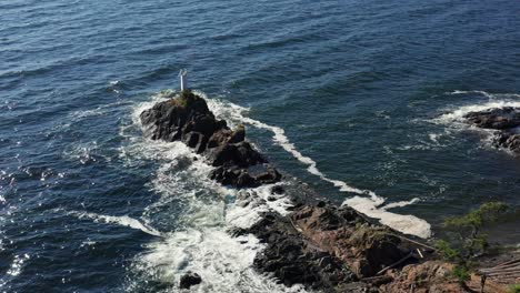 Waves-crashing-on-the-shoreline-next-to-a-lighthouse---Drone-Aerial-Shot