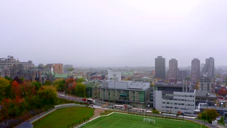 Drone-moving-up,-over-a-synthetic-soccer-field-in-the-middle-of-the-city-on-a-foggy-fall-morning-in-Montreal