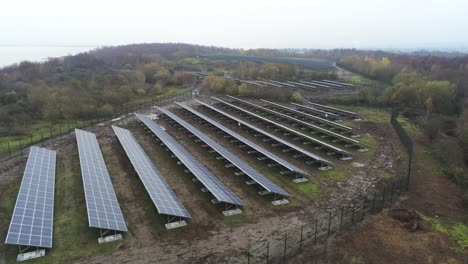 Solar-panel-array-rows-aerial-view-misty-autumn-woodland-countryside-low-orbit-right