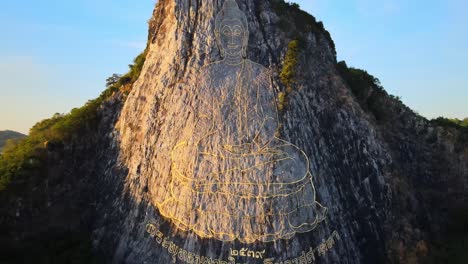 4k-Aerial-Pan-up-above-the-Buddha-Mountain-in-Pattaya-at-Sunrise,-golden-light-on-the-image-of-Buddha-in-Khao-Chi-Chan,-Chonburi,-Thailand