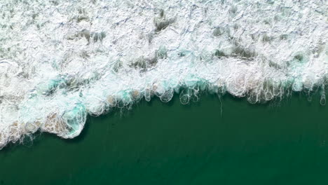 Drone-shot-starting-on-breaking-waves-rising-to-wide-shot-of-shoreline