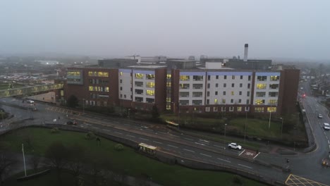 Misty-foggy-hospital-building-UK-town-traffic-aerial-view-low-angle-dolly-right
