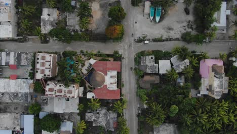 Birds-eye-view-Descending-shot,-Scenic-view-house-and-highway-crossing-of-Isla-Holbox,-Mexico,-cars-passing-by-the-road-in-the-background