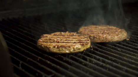 Smoke-surrounds-flame-grilled-burgers,-hamburgers-sizzle-on-grill,-slider-slow-motion