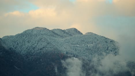 timelapse-of-clouds-flying-over-a-snowy-mountain-top,-covering-the-trees-with-a-freezing-wind,-everything-is-turning-white