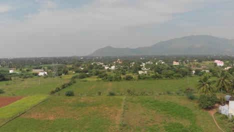 Aerial-flyover-above-an-Indian-village-surrounded-by-green-nature-forest-and-huge-mountains-in-the-middle-of-the-frame