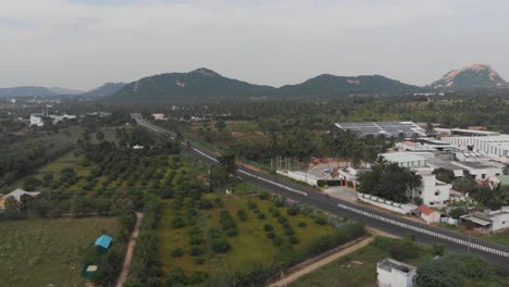 Flying-over-a-highway-in-India-surrounded-by-lush-green-fields-and-mountains-in-the-background-covered-in-greens