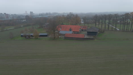 Aerial-track-of-small-farm-with-mist-covered-city-sky-line-in-the-background