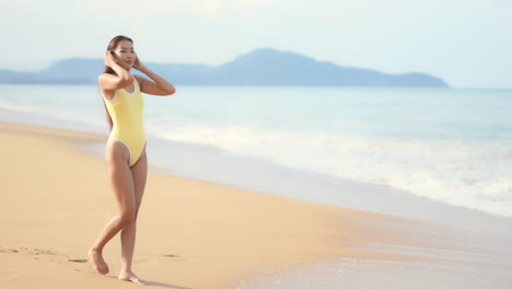 A-pretty-young-woman-walks-along-a-golden-sandy-beach-as-the-surf-rolls-in