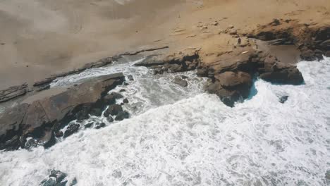 Foamy-Sea-Water-Splashing-Against-Rocky-Shore-In-Lobitos-Beach,-Peru-During-Sunny-Day-Of-Summer---aerial-drone-shot
