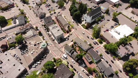 A-daytime-birds-eye-drone-view-of-a-suburban-downtown-traffic-grid-among-the-buildings-and-shops,-cars-and-other-vehicles-driving-on-the-roadway