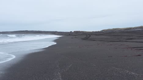 Low-flying-aerial-at-shore-of-Sandvik-beach-with-volcanic-black-sand-in-Iceland